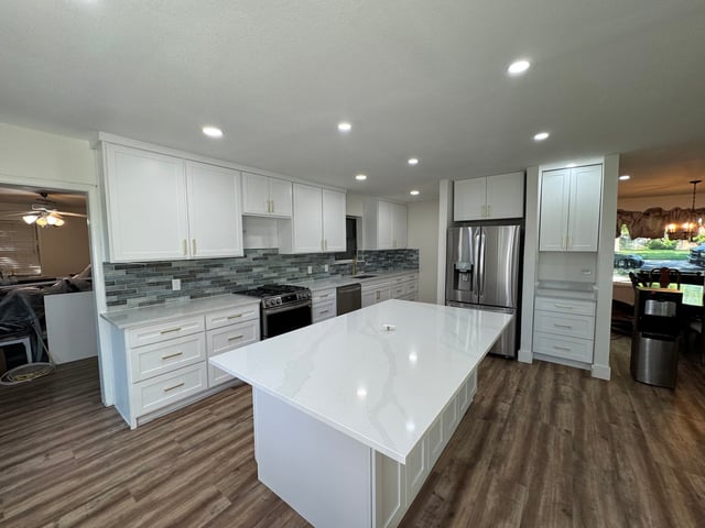 Remodeled kitchen with white shaker cabinets, quartz island and glass tile backsplash